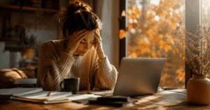 Überforderte Frau am Laptop mit herbstlichem Licht und stressigem Arbeitsplatz als Symbol für innere Unruhe, Angststörung Symptome und Stressbewältigung