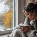 Warum Dauerstress dein Immunsystem schwächt – und was du dagegen tun kannst Erschöpfte Frau sitzt mit einer Tasse Tee am Fenster und blickt müde nach draußen. Das Bild symbolisiert Dauerstress, Erschöpfung, innere Unruhe und ein geschwächtes Immunsystem.